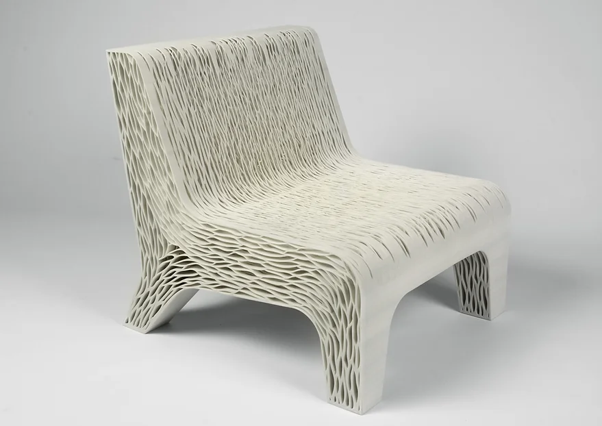 A imagem mostra uma cadeira feita com impressão 3D. Ela é branca e tem diversos orifícios ao longo de sua estrutura.